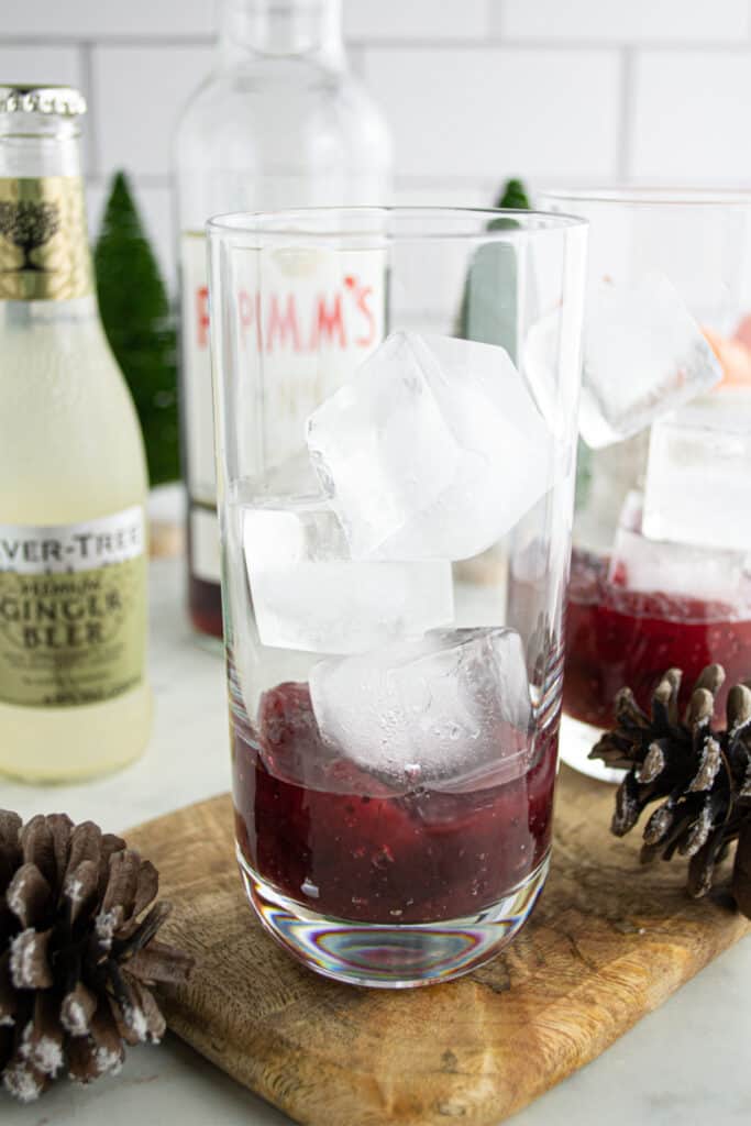 Tall glass with cranberry sauce and ice cubes being prepared for a Cranberry Pimm’s Cocktail.