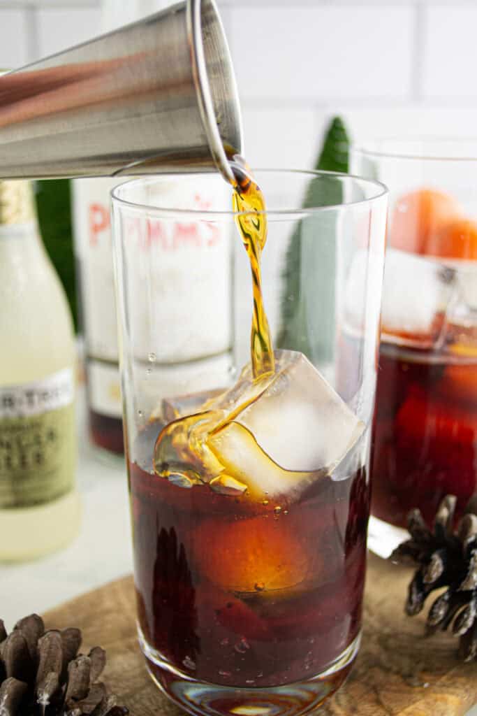 Pouring Pimm’s liqueur into a glass filled with ice and cranberry sauce to make a Cranberry Pimm’s Cocktail.