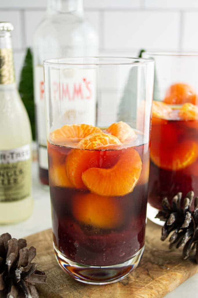 Adding peeled clementine slices to the Cranberry Pimm’s Cocktail in a tall glass.