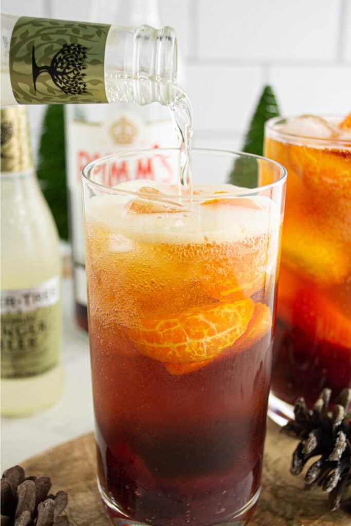 Pouring ginger beer over the cranberry, clementine, and Pimm’s mixture to finish the Cranberry Pimm’s Cocktail.