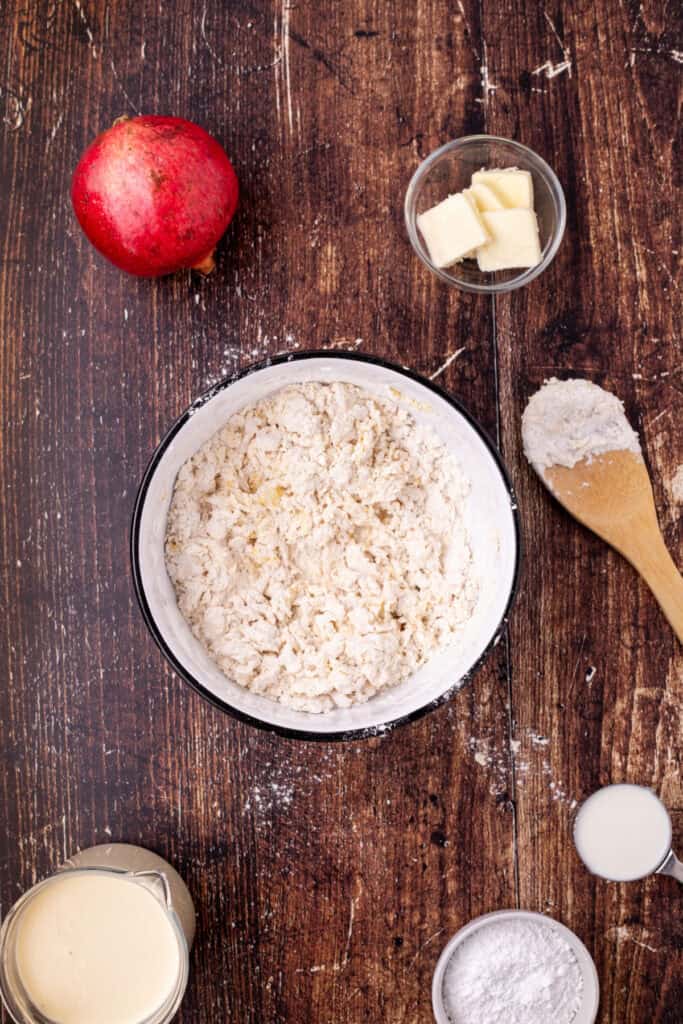 Mixing bowl showing flour and eggs partially mixed into a rough dough with wooden spoon and ingredients nearby.