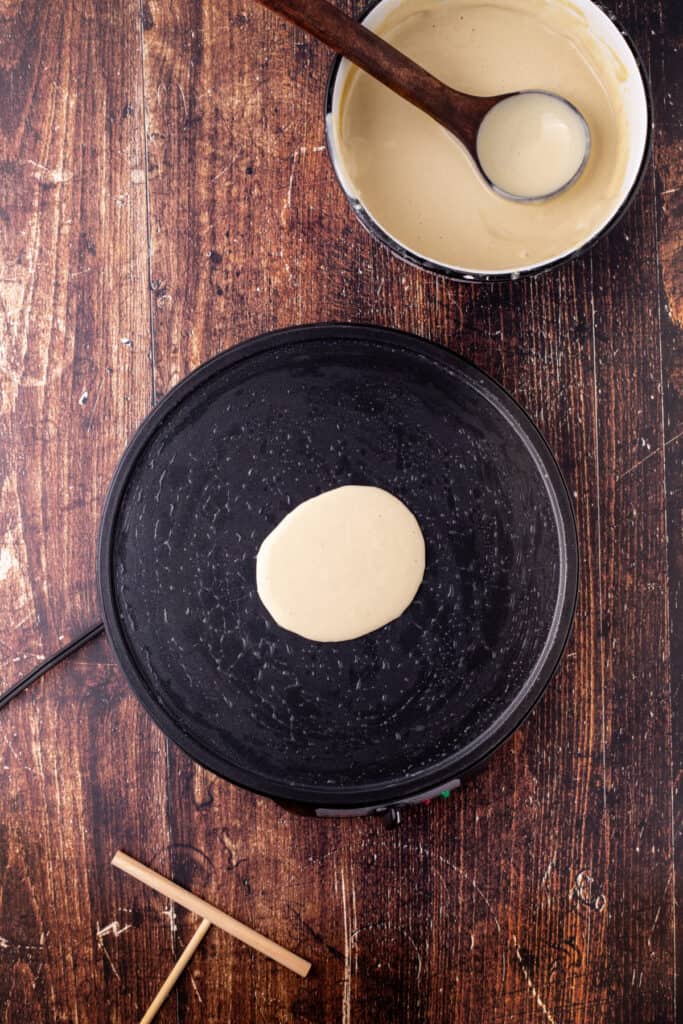 A small amount of eggnog crepe batter poured onto the center of the pan, ready to spread for cooking.