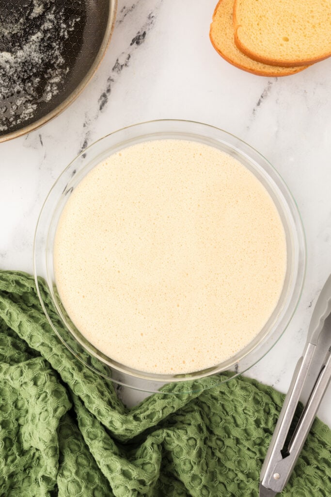 Pie plate filled with blended eggnog mixture set beside buttered skillet and bread slices.
