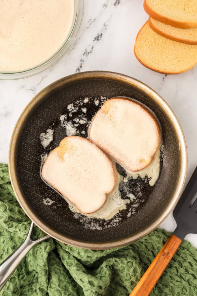 Bread slices cooking in buttered skillet until golden for Eggnog French Toast.