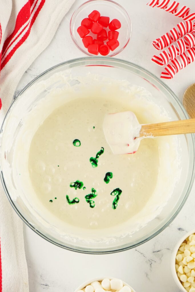 A bowl of melted marshmallow mixture with drops of green food coloring added before stirring.
