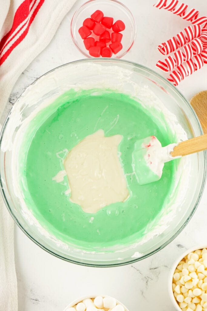 Green tinted marshmallow mixture in a mixing bowl with melted white chocolate being folded in.