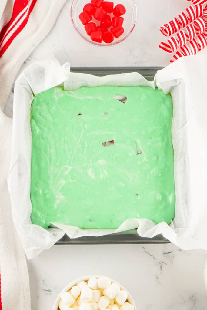 Green nougat mixture spread evenly in a parchment lined baking pan before adding toppings.