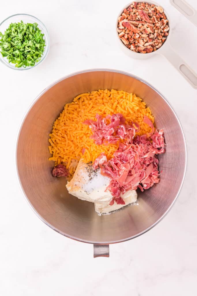 Mixing bowl filled with shredded cheddar, cream cheese, and chopped prosciutto ready to be blended for Holiday Cheese Ball.