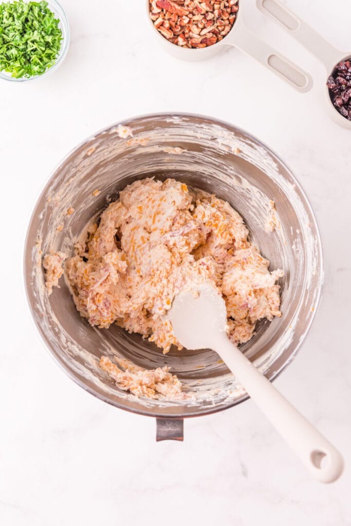 Mixed cheese and prosciutto filling in a stainless steel bowl with a spatula, showing texture of the Holiday Cheese Ball mixture.