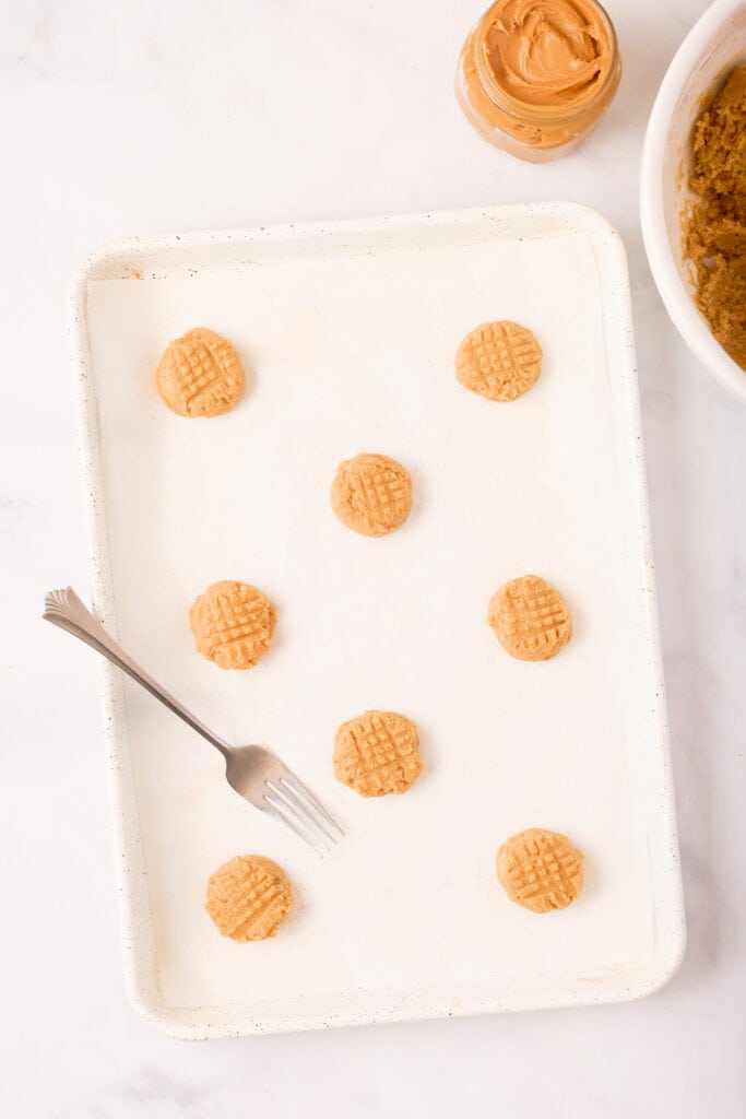 Peanut butter cookie dough on a baking sheet with visible fork-pressed crisscross patterns before baking.