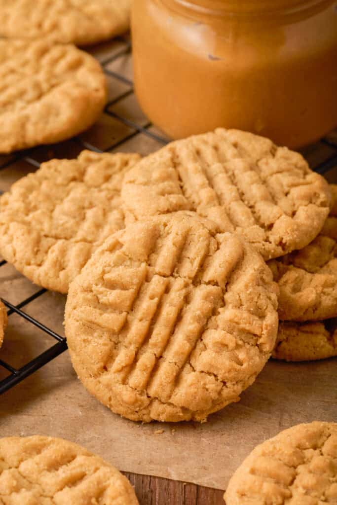 Stack of soft peanut butter cookies cooling near a jar of peanut butter and a red-striped kitchen towel.