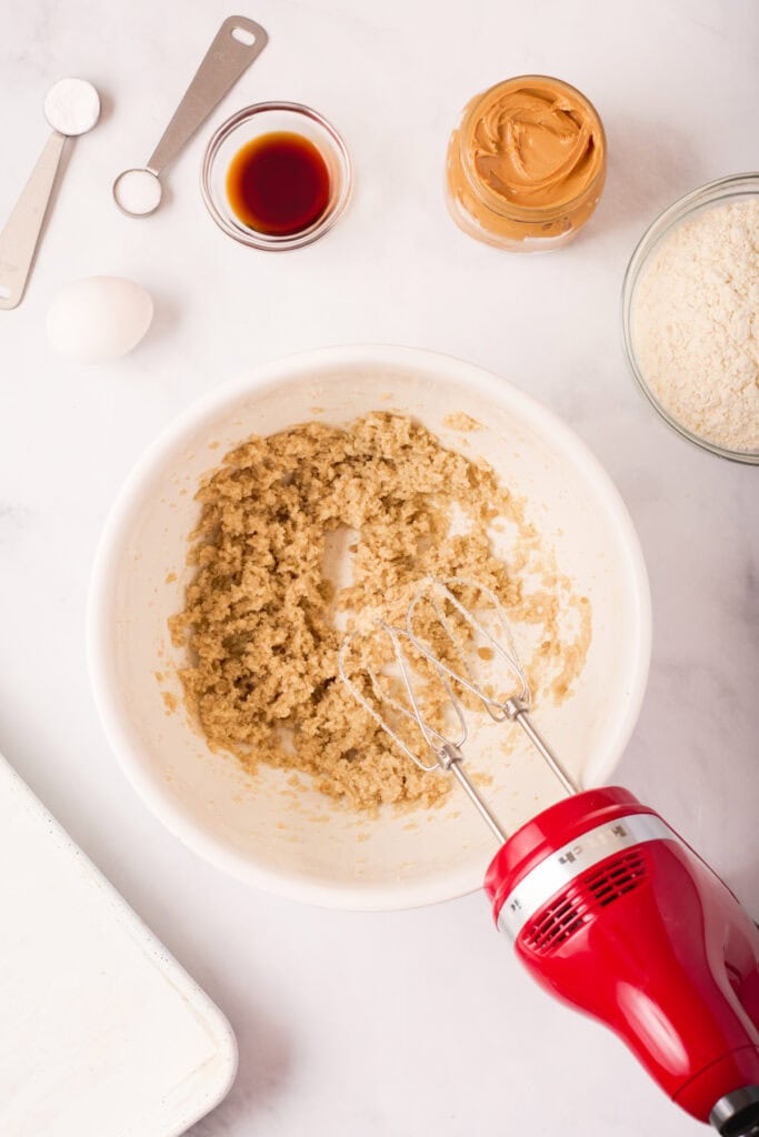 Creamed butter, shortening, and sugars mixed together in a white bowl with a red hand mixer resting nearby.