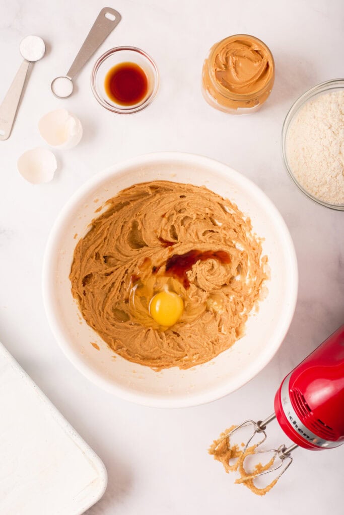 Egg and vanilla extract added to the peanut butter dough before final mixing, with a red hand mixer nearby.