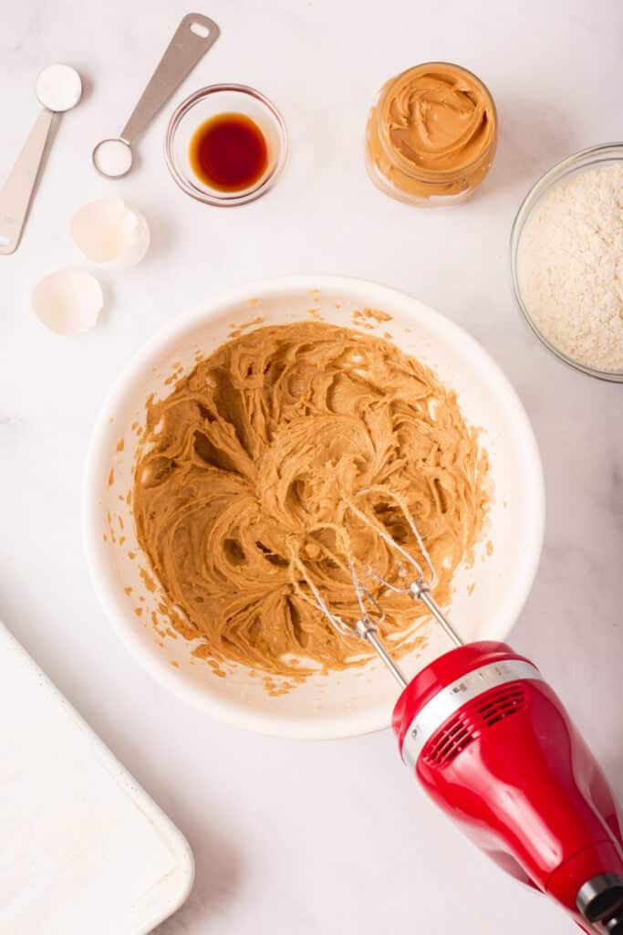 Fully combined peanut butter cookie batter, light brown and creamy in texture, shown in a mixing bowl with the hand mixer resting beside it.