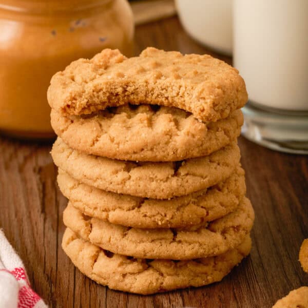 Square image of a stack of peanut butter cookies with a bite taken out of the top one, showing soft texture and golden color.