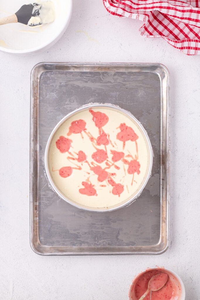 Dollops of pink peppermint batter scattered on top of the cheesecake batter before swirling.