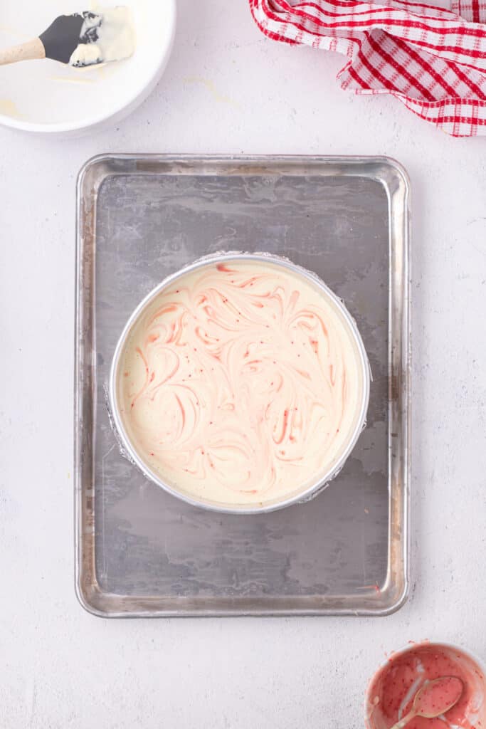Cheesecake batter swirled with pink peppermint mixture, creating a marbled pattern before baking.
