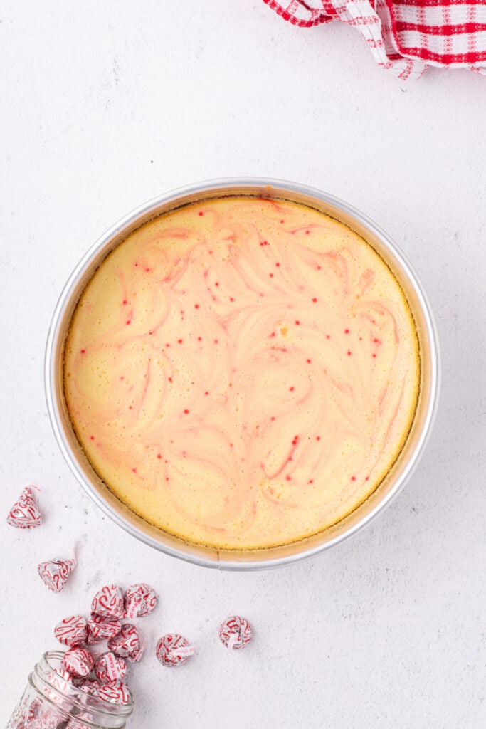 Close view of the baked peppermint eggnog cheesecake with visible pink swirls and candy cane Kisses scattered nearby.