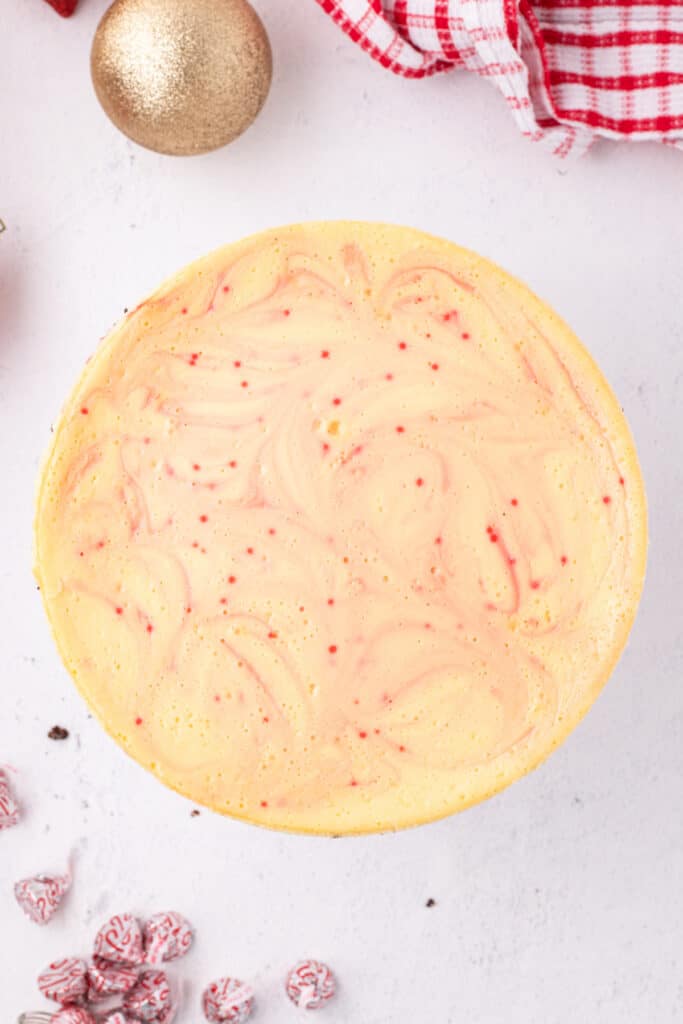 Overhead shot of the baked cheesecake decorated lightly with peppermint swirls, holiday ornaments, and candy cane Kisses.