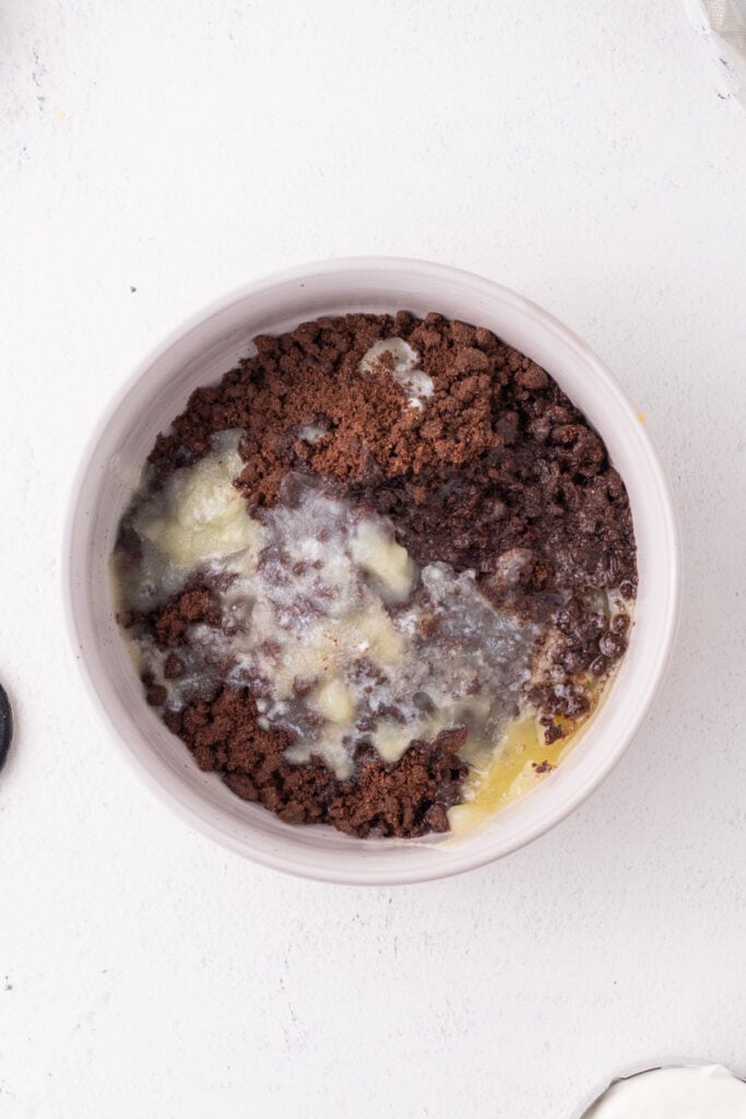 Bowl of chocolate graham cracker crumbs mixed with melted butter, showing the start of the crust mixture for the peppermint eggnog cheesecake.