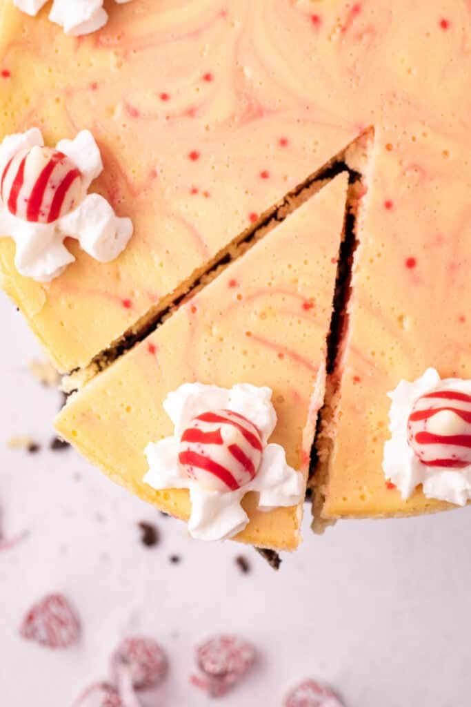Slice of peppermint eggnog cheesecake being lifted from the whole cake, showing the whipped cream and peppermint Kiss garnish.