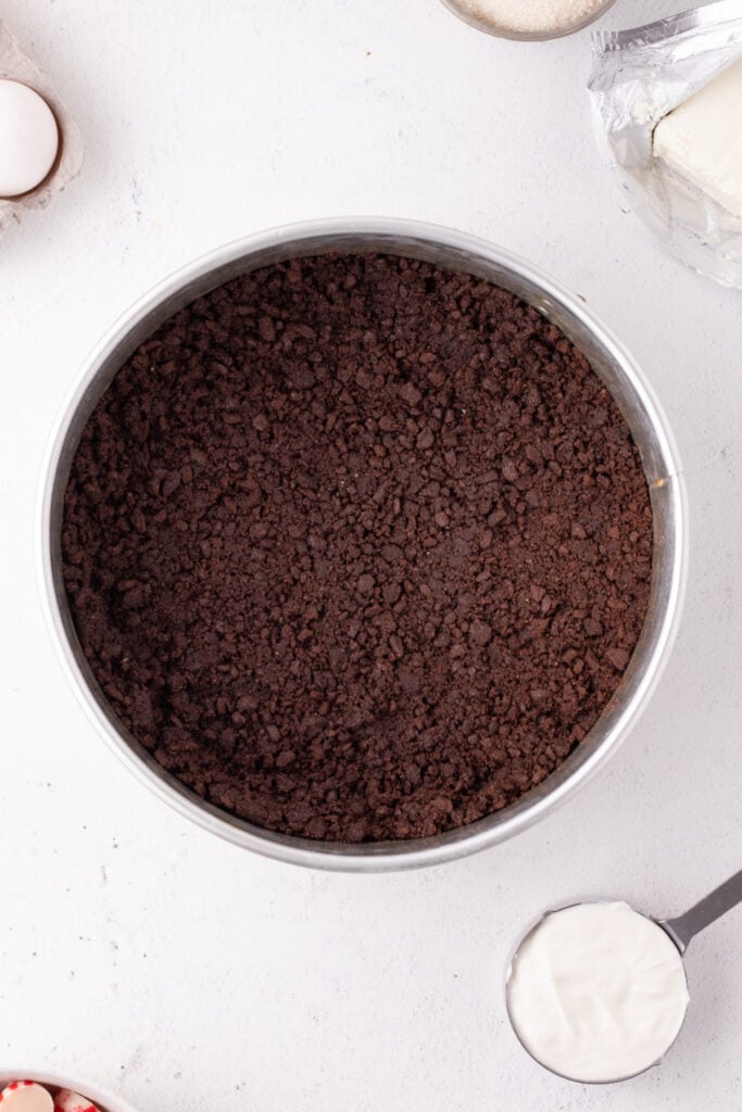 Pressed chocolate graham cracker crust spread evenly in a springform pan, ready to bake for the peppermint eggnog cheesecake.