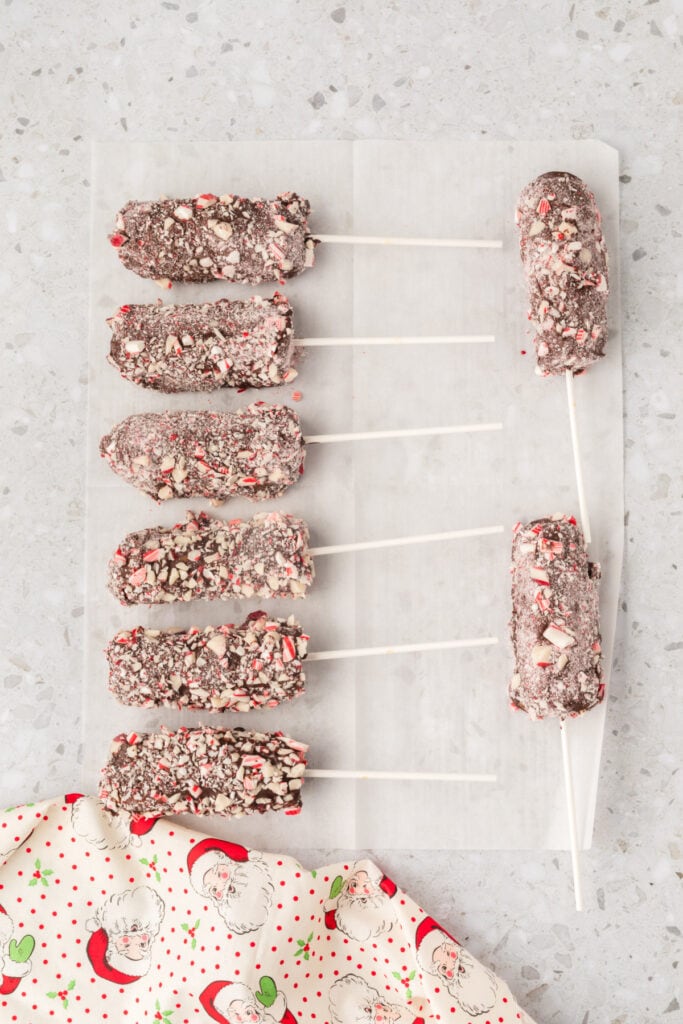 Finished peppermint marshmallow wands coated in peppermint pieces and set on parchment paper to cool.
