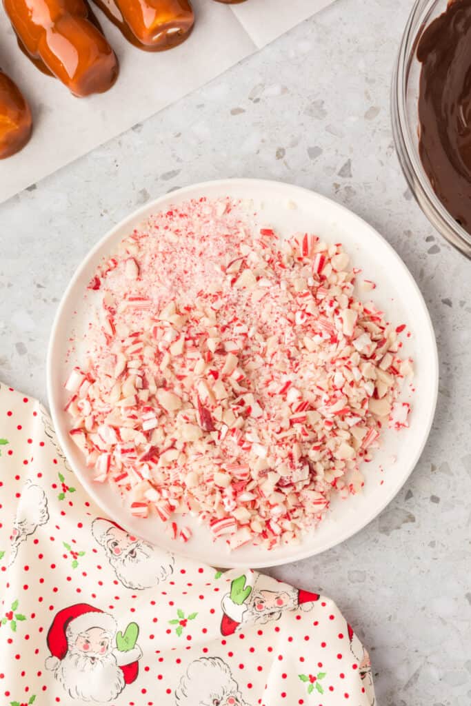 A plate of crushed peppermint candy in various sizes, ready for coating the chocolate dipped marshmallow wands.