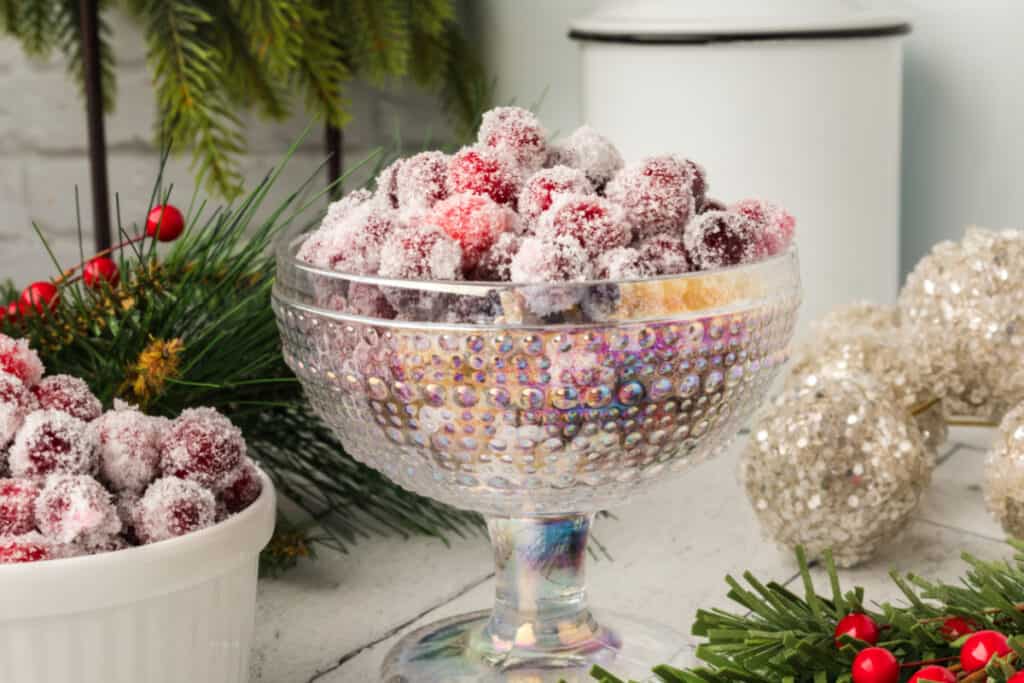 Close-up of sugared cranberries in a decorative glass dish, surrounded by holiday decor and gold ornaments.
