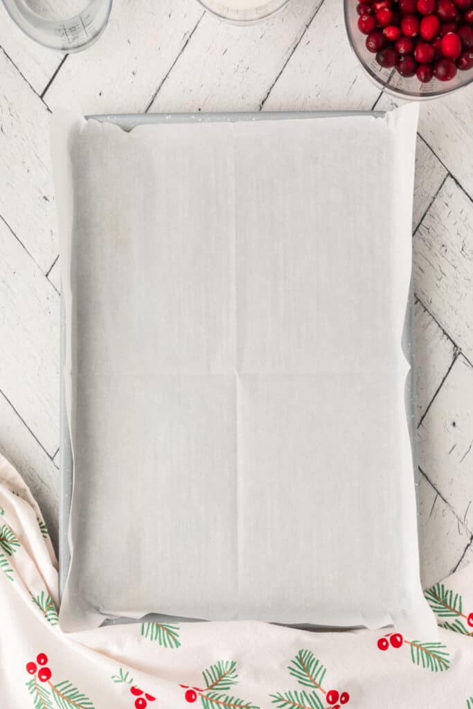 Baking sheet lined with parchment paper, ready for drying sugared cranberries, surrounded by ingredients.