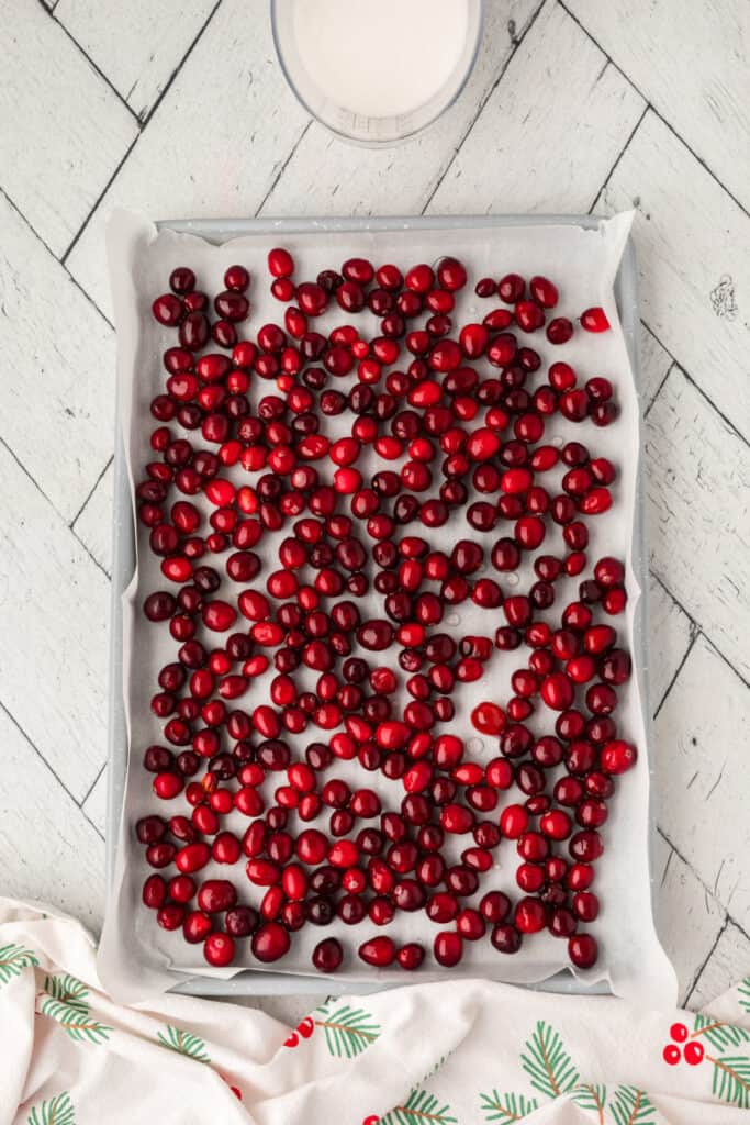 Cranberries spread out on a parchment-lined baking sheet to dry after being coated in syrup.