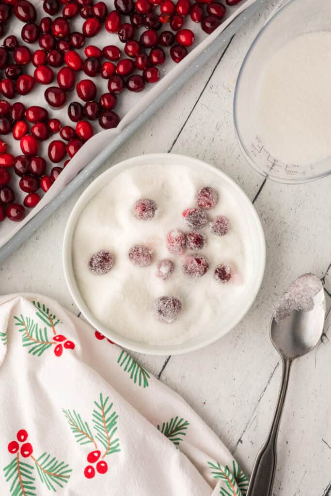 Cranberries being rolled in granulated sugar in a white bowl for the final coating step.