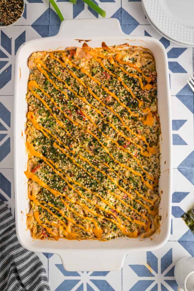 Baked sushi casserole in a white dish topped with furikake and drizzled with sriracha mayo, ready to serve.