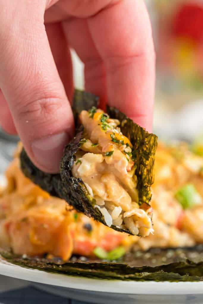Hand holding a bite of sushi bake wrapped in a piece of nori seaweed for serving.
