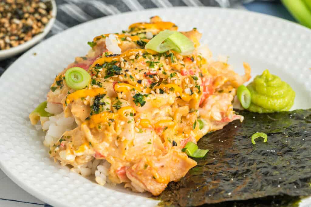 Sushi bake served with nori and wasabi on a white plate, topped with green onions and sesame seasoning.