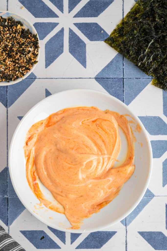 Sriracha mayo mixture swirled together in a bowl, forming a creamy orange sauce for drizzling.