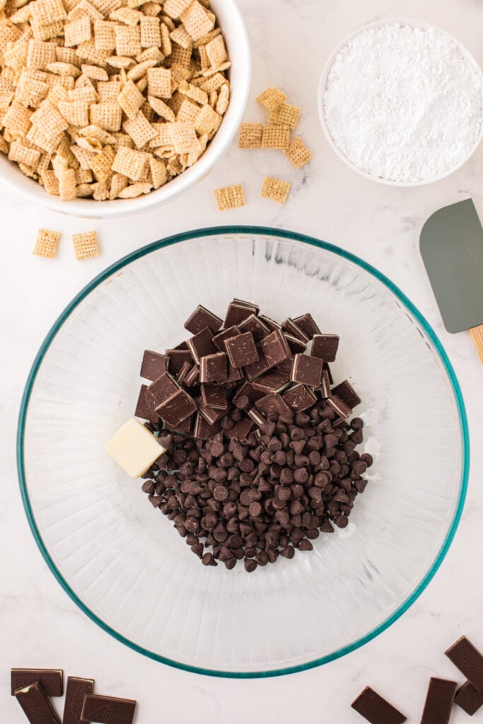Large glass bowl filled with chocolate chips, chopped Andes mints, and a piece of butter before melting.