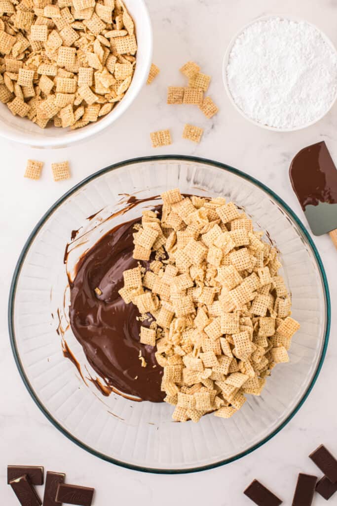 Melted chocolate mixture in a large bowl with Rice Chex cereal poured on top, ready to be folded together.
