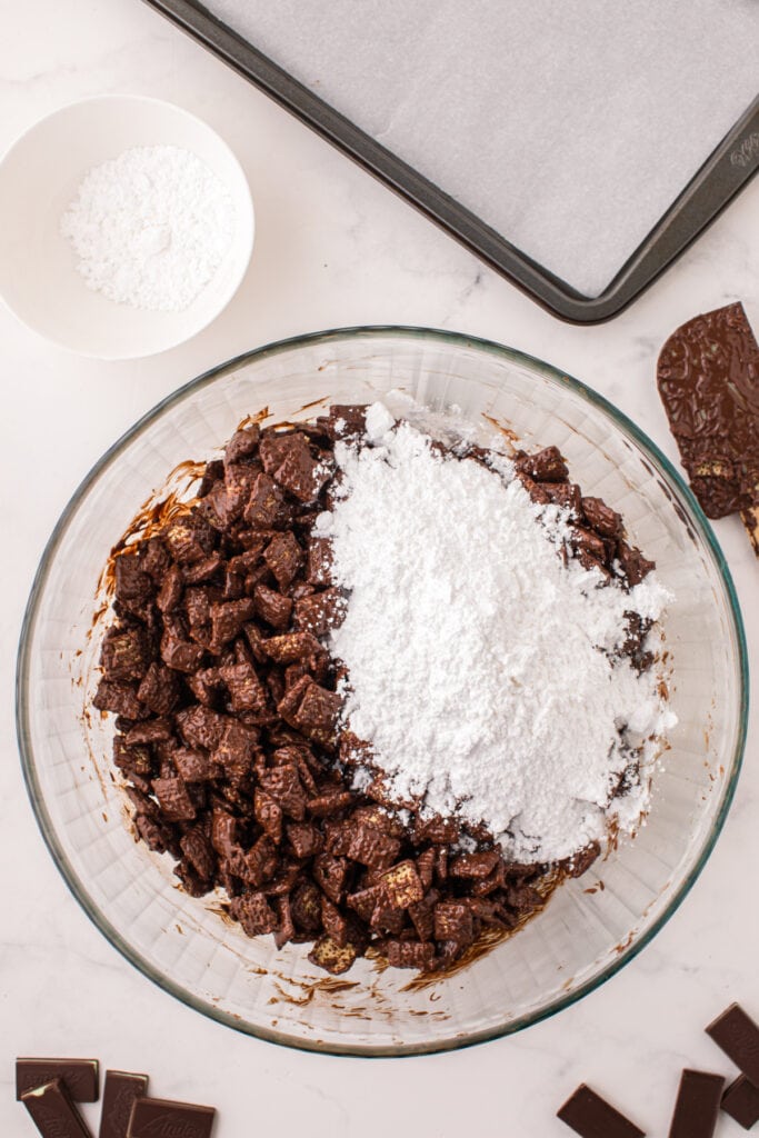 Powdered sugar added on top of chocolate coated cereal in a mixing bowl before shaking to coat.