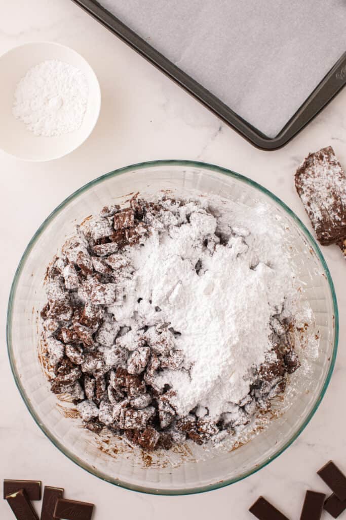 Half mixed bowl of powdered sugar and chocolate coated cereal showing the coating process.
