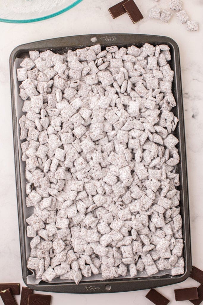 Large baking sheet lined with parchment paper covered in freshly coated Thin Mint Muddy Buddies.