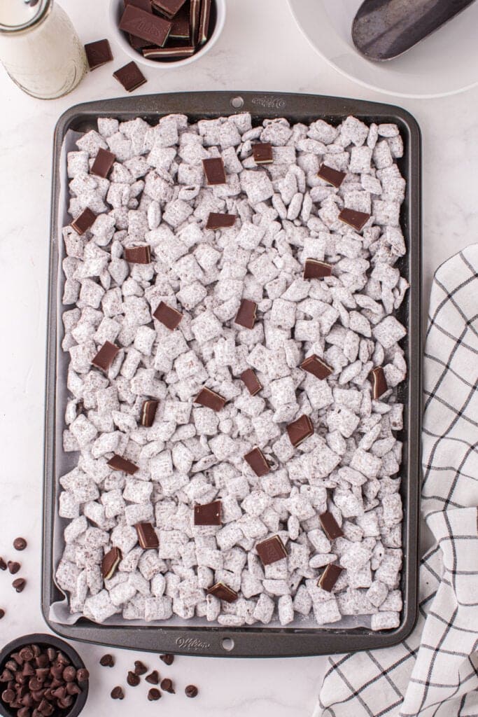 Close view of Thin Mint Muddy Buddies spread on a baking sheet with extra Andes mint pieces on top.