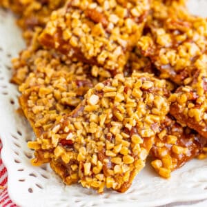 square close up of toffee graham cracker pralines stacked on a white serving plate with crunchy toffee bits and pecans