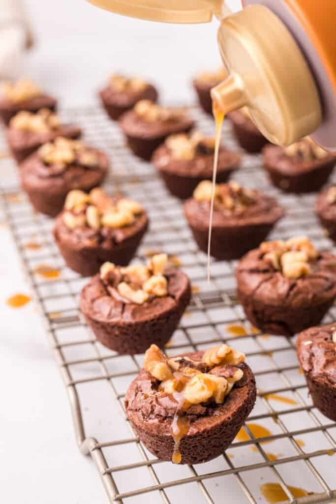 Close up of turtle brownie bites on a cooling rack while caramel is being drizzled over the tops.