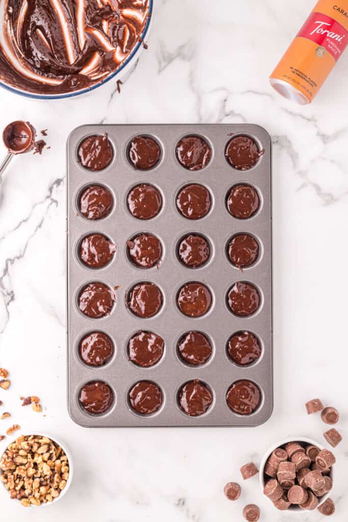 Mini muffin pan filled with spooned brownie batter, shown alongside the mixing bowl, scoop, walnuts, and Rolos.