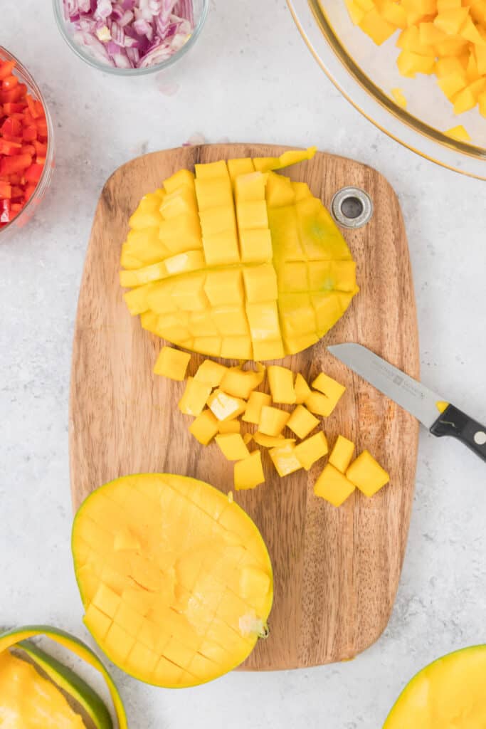 Fresh mango halves sliced in a grid pattern on a cutting board with diced mango pieces and a paring knife.