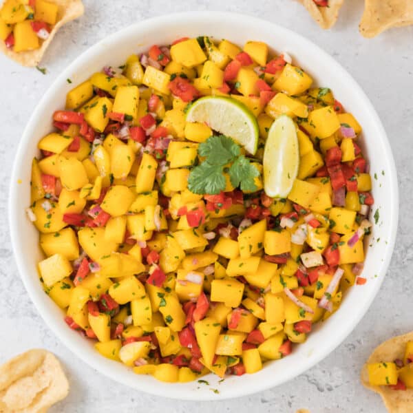Close up overhead shot of mango salsa in a white bowl with lime wedges and cilantro on top.