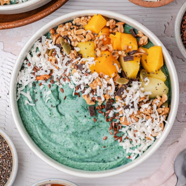 Square-cropped blue spirulina smoothie bowl with colorful fruit and coconut toppings on a light background.