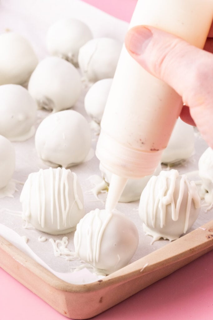 Drizzling white chocolate over cake truffles before adding sprinkles
