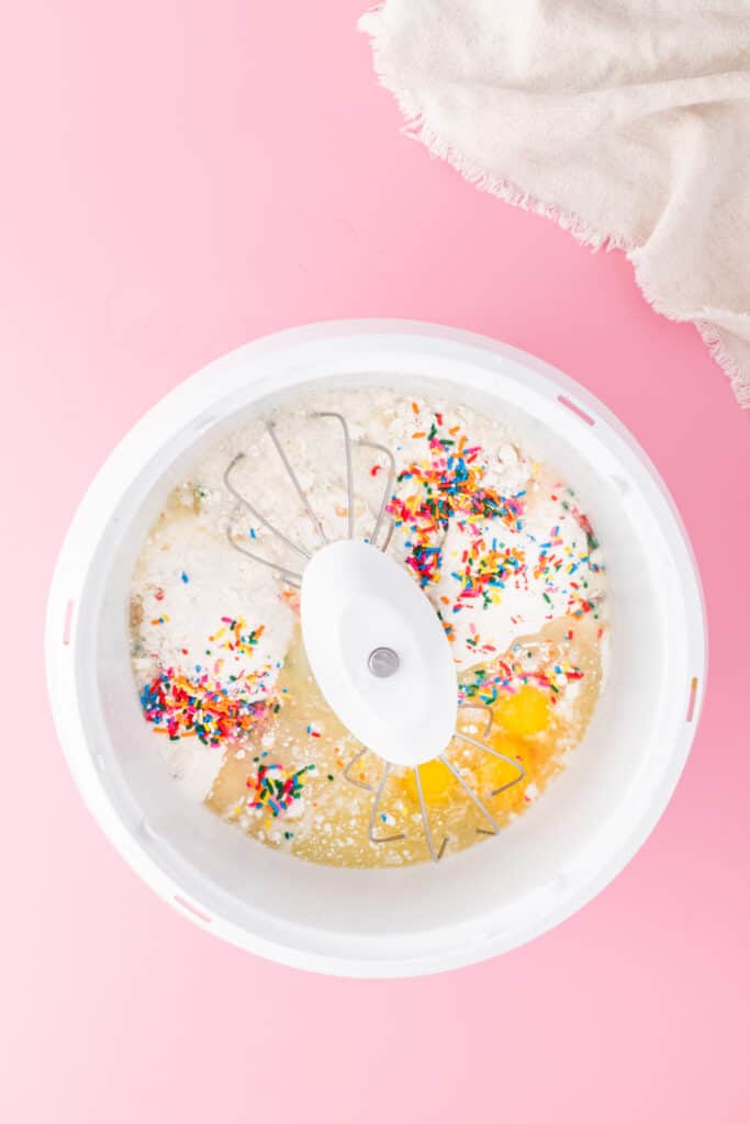 Cake mix, eggs, oil, water, and sprinkles in a mixing bowl ready to be mixed